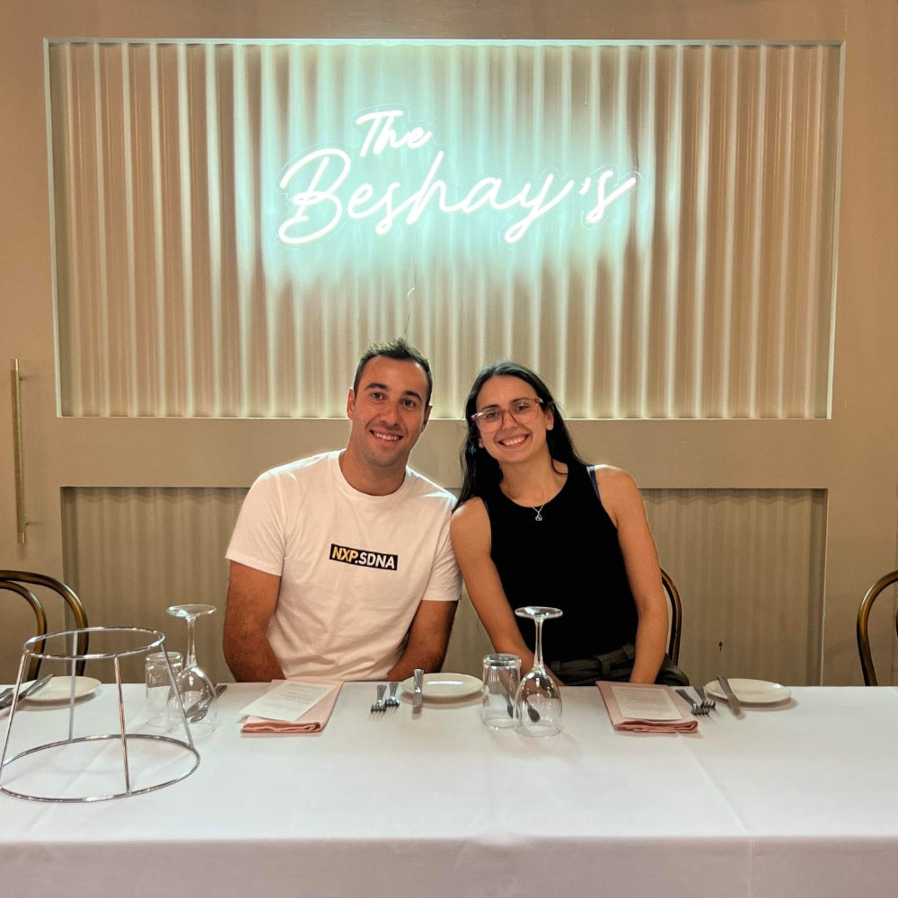 Couple sitting at a dining table with a glowing light sign in the background, creating a cozy and romantic ambiance