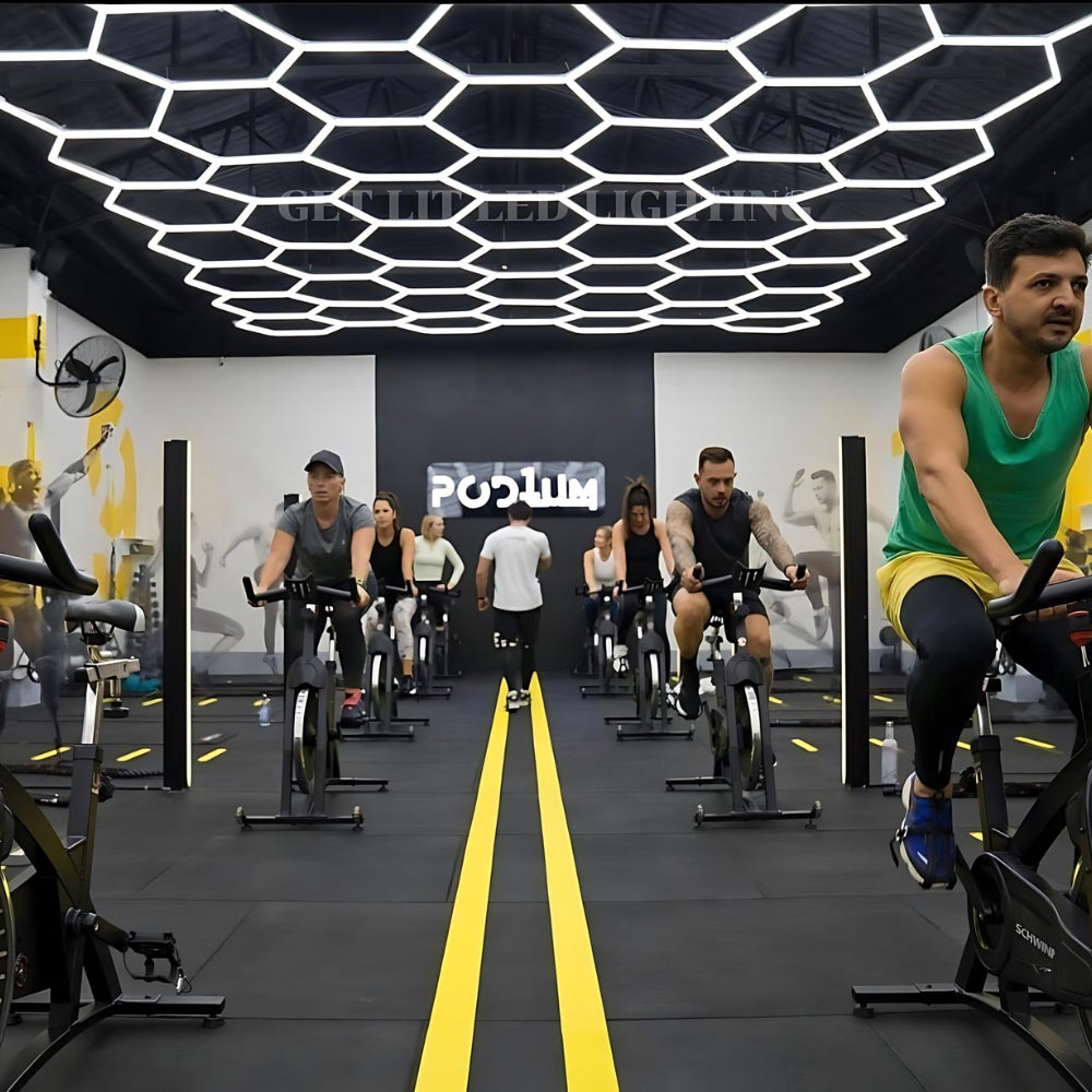 People cycling in a gym under a ceiling with hexagon LED grid lights, enhancing the workout environment