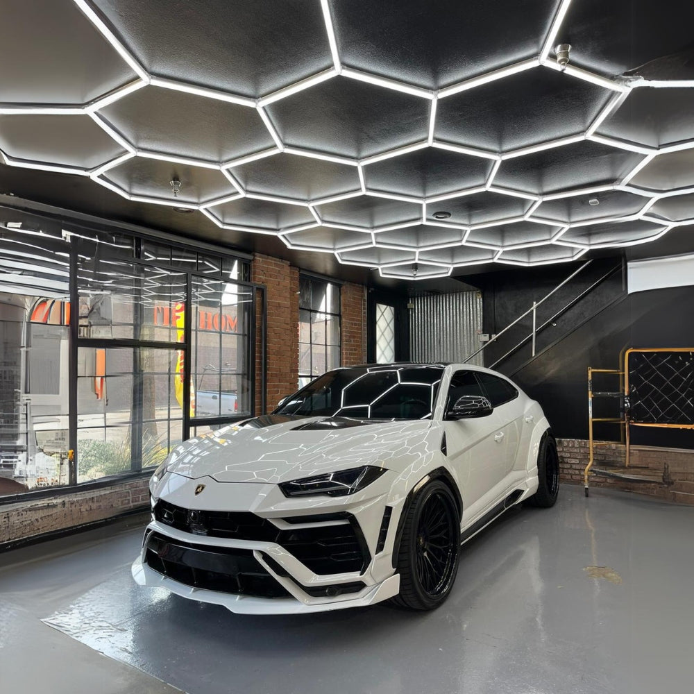 White car parked under a ceiling with white hexagon LED grid lights, creating a sleek and modern lighting effect