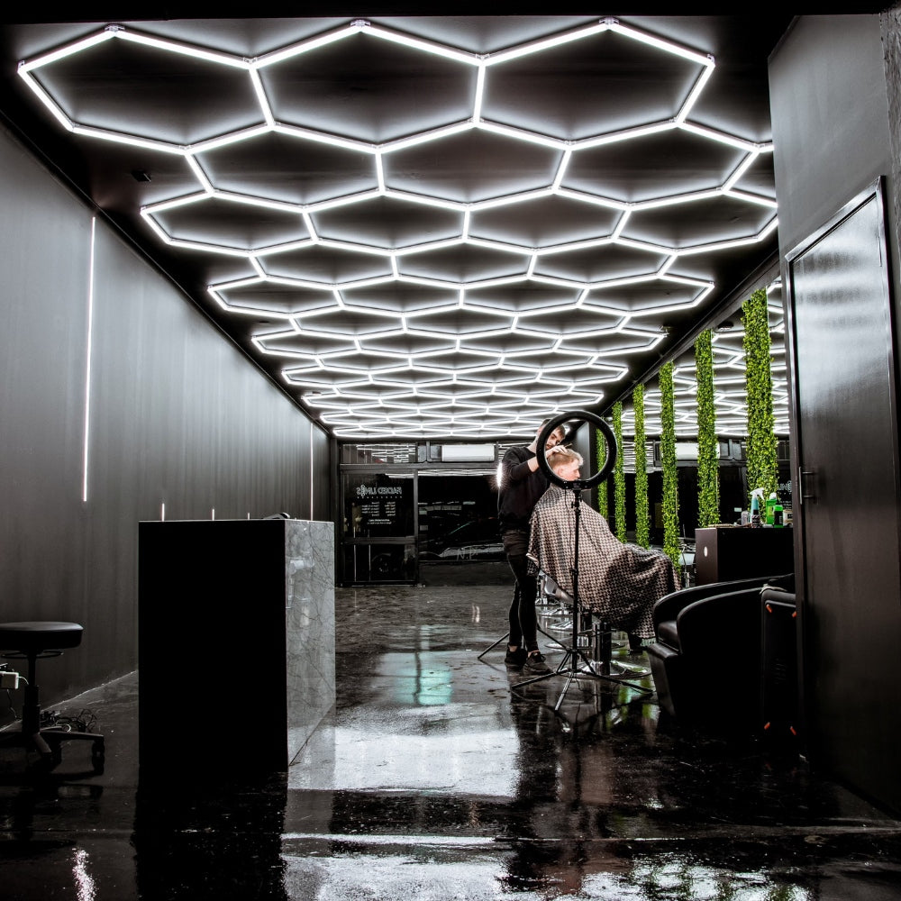 Hair salon scene with a stylist working on a client, under the bright and modern hexagon LED grid lights overhead